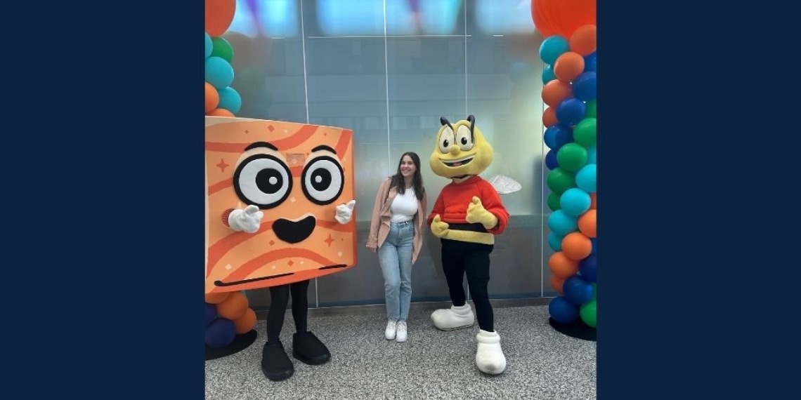 Woman with brown hair smiling next to costumed characters of a bee and animated cereal piece.